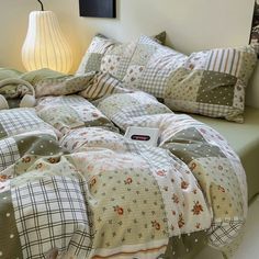 an unmade bed with many pillows and blankets on it in a room next to a lamp