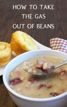 a white bowl filled with soup next to muffins on a wooden table and text overlay reads how to take the gas out of beans