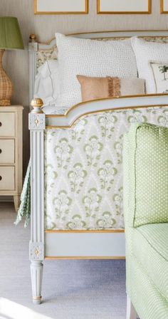 a white bed sitting next to a green chair in a room with pictures on the wall