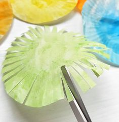 paper plates and scissors on a table with colored paper flowers in the middle, one being cut into smaller pieces