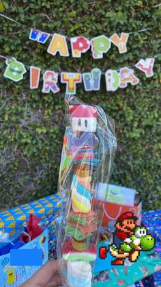 a person holding up a birthday cake in front of a table with mario and luigi party decorations