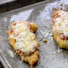 two pieces of chicken covered in cheese and sauce on a baking sheet with grated parmesan