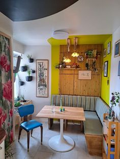 a dining room table with blue chairs and yellow walls in the background, next to a wooden bench