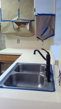 a kitchen sink with blue tape on the counter top and cabinets in the back ground