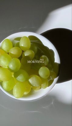 a white bowl filled with green grapes sitting on top of a table next to a shadow