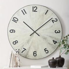 a clock on the wall above a shelf with books and vases next to it