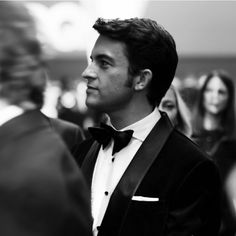 a man in a tuxedo looks off into the distance as people look on