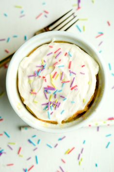 a white bowl filled with frosting and sprinkles next to a fork