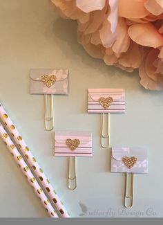 three pink and gold paper clips with hearts on them, attached to the side of each other