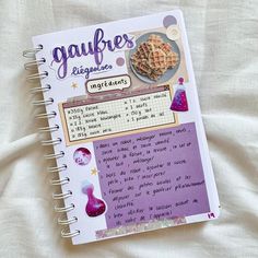 a recipe book is open on a white sheet with purple writing and images of food