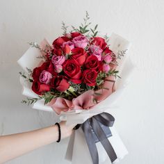 a person holding a bouquet of red and pink roses in their hand with ribbon around it