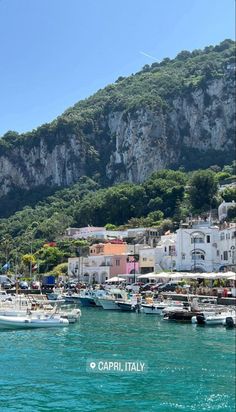 several boats are docked in the water near some mountains and houses on top of a hill