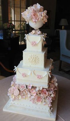 a three tiered wedding cake with pink flowers on the top and bottom, sitting on a table in front of a window