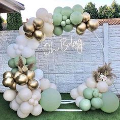 a balloon arch with gold and white balloons on the grass in front of a brick wall