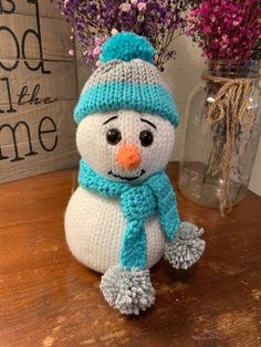 a knitted snowman sitting on top of a wooden table next to purple flowers