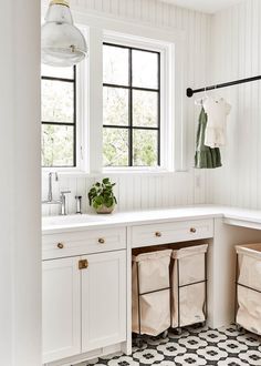 a kitchen with white cabinets and black and white tile flooring that has three bins in front of the sink