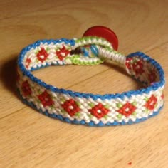 a blue and white bracelet with red flowers on it sitting on a wooden table next to a button