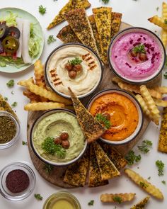 various dips and sauces are arranged on a platter with pita chips