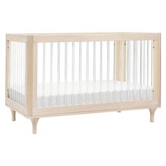 a baby crib with white sheets and wood trims on the bottom, in front of a white background