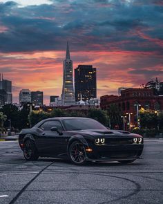 a black sports car parked in front of a cityscape at sunset with the sun setting