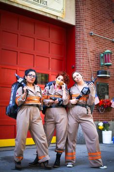 three women dressed in orange and brown posing for the camera with backpacks on their shoulders