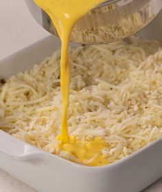 someone pouring cheese sauce on top of rice in a pan