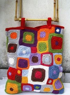 a multicolored crocheted bag hanging on a wall with a bamboo handle