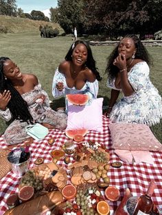 three women sitting at a picnic table with food on it and one woman holding her hand up to her mouth