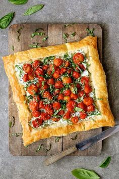 a square pizza topped with tomatoes and cheese on top of a cutting board next to a knife