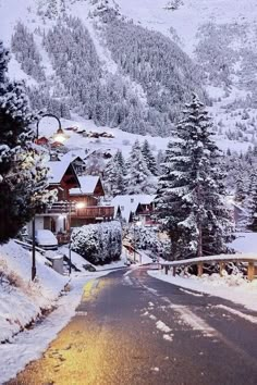 a snowy mountain with houses and trees in the foreground, at night on a cold winter's day