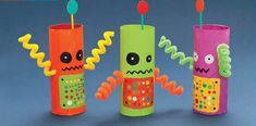 three different colored cups with toothbrushes sticking out of them, one is decorated like a monster and the other has an alien face