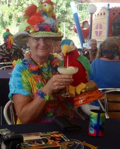 a woman wearing a colorful hat and holding a drink in her hand while sitting at a table