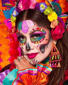 a woman with colorful makeup and flowers on her face posing for a photo in front of an orange background