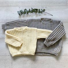 three sweaters laid out next to each other on a wooden floor with eucalyptus leaves