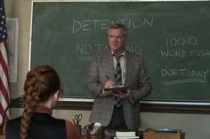 a man standing in front of a blackboard with writing on it and an american flag behind him