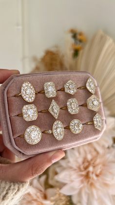 a hand holding a pink velvet case with lots of diamond studs on it and a bouquet of flowers in the background