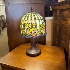 a stained glass lamp sitting on top of a wooden table next to a dresser in a store