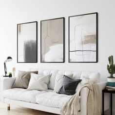 a living room with white furniture and three paintings on the wall above it's couch