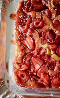 a square cake covered in strawberries and other toppings on top of aluminum foil