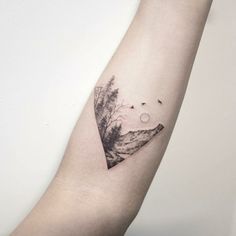 a small triangle tattoo on the left arm with birds flying over it and trees in the background