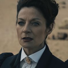 a woman wearing a suit and tie standing in front of a sandy area with no people