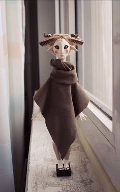 a stuffed animal dressed in a brown cape and boots standing on a window sill