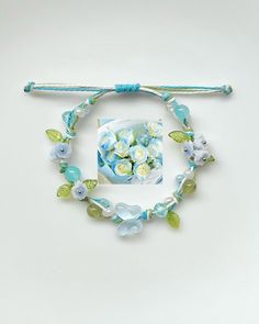 a bracelet with flowers and leaves is shown on a white surface, next to a stick