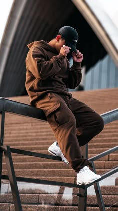 a young man sitting on top of a metal rail next to stairs wearing a black hat