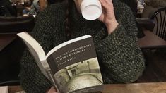 a woman drinking from a cup while reading a book