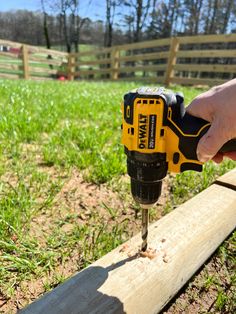 a person using a drill to attach a piece of wood on the ground in front of a fence