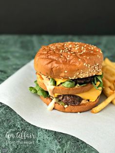 a hamburger with cheese and lettuce next to french fries on a paper towel