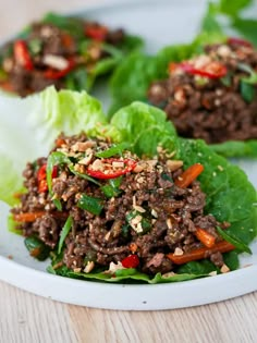 lettuce wraps filled with meat and vegetables on a white plate, ready to be eaten