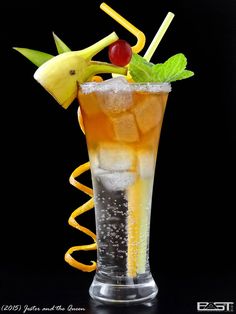 a tall glass filled with ice and fruit on top of a black table next to a yellow spiral