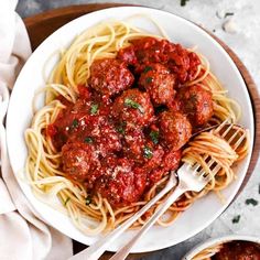 spaghetti and meatballs on a white plate with two bowls of sauce in the background